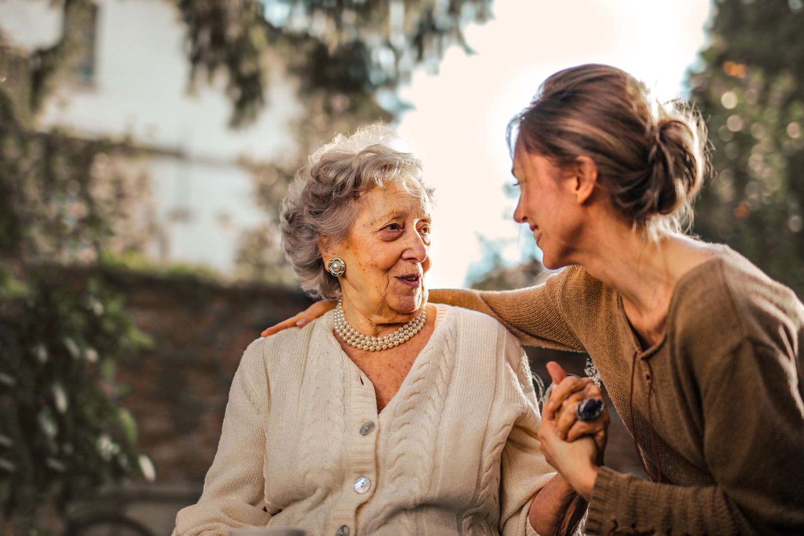 A smiling older woman and her adult daughter holding hands together outdoors